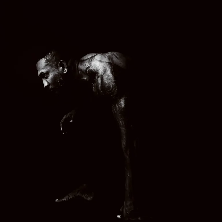 Low-key black and white study of a muscular figure crouching in darkness